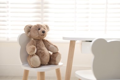 Cute teddy bear on chair in child's room. Space for text