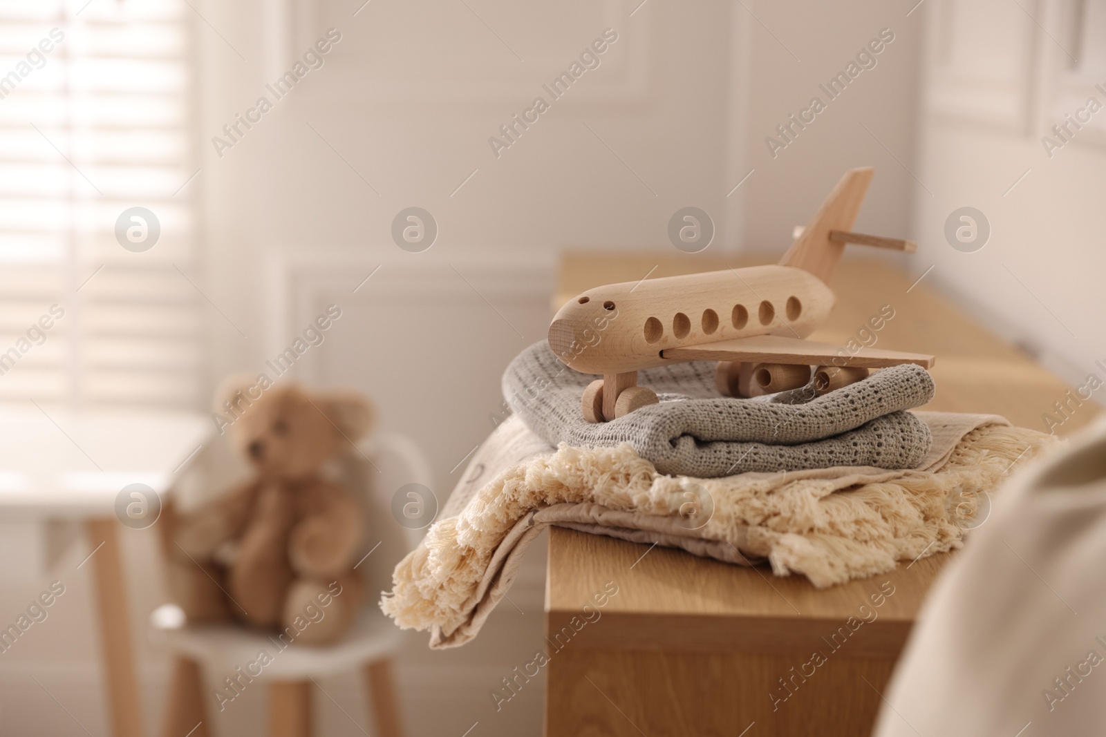 Photo of Toy plane and blankets on chest of drawers in child's room. Space for text