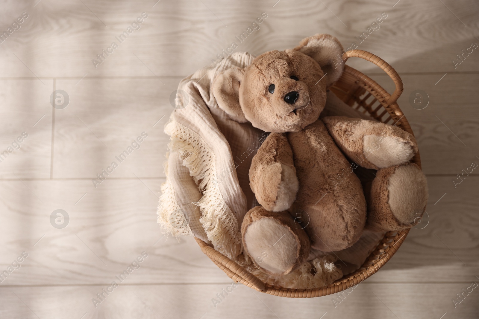 Photo of Cute teddy bear in basket on floor, top view. Space for text