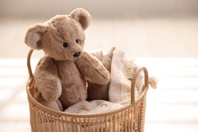 Cute teddy bear in basket on floor, closeup