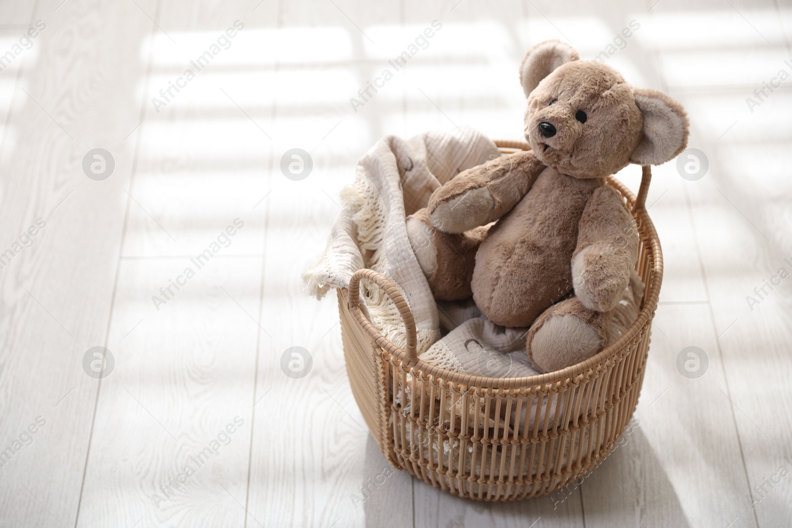 Photo of Cute teddy bear in basket on floor. Space for text