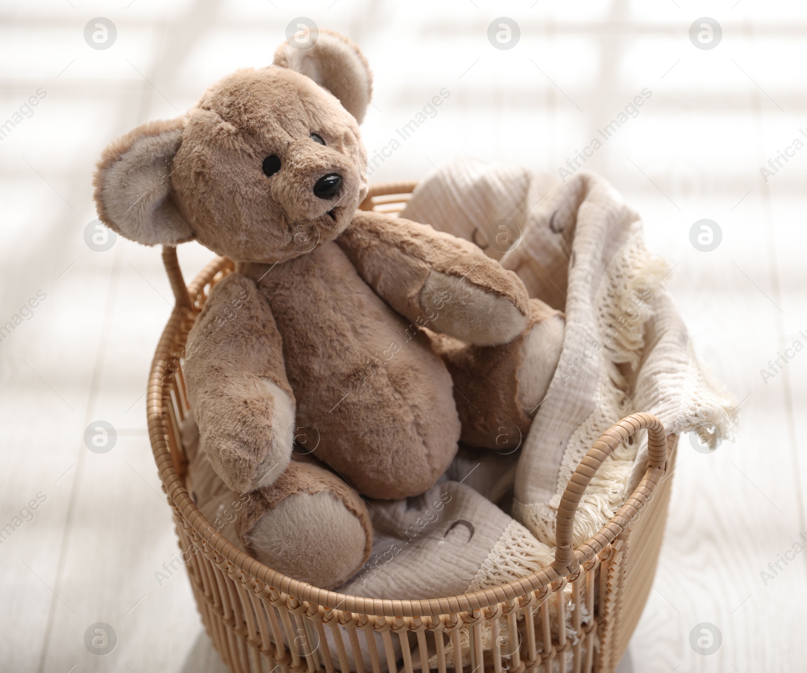 Photo of Cute teddy bear in basket on floor, closeup