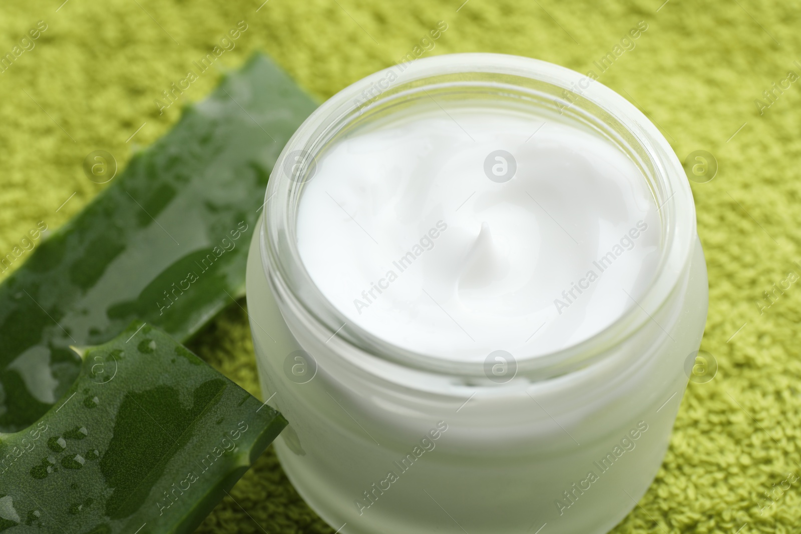 Photo of Cream and aloe leaves on green background, closeup