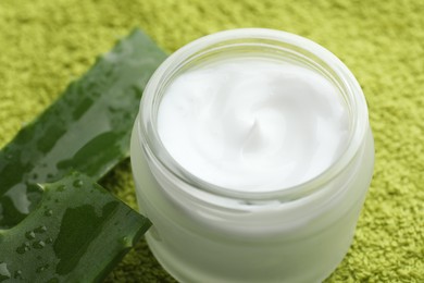 Photo of Cream and aloe leaves on green background, closeup