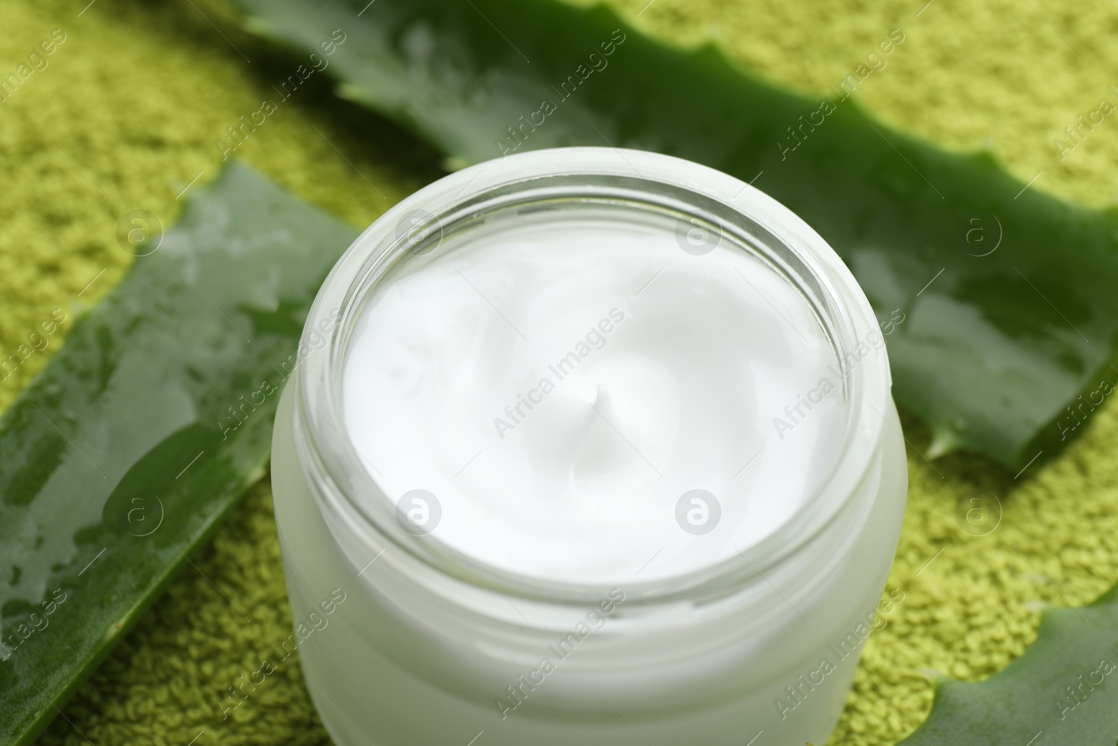 Photo of Cream and aloe leaves on green background, closeup