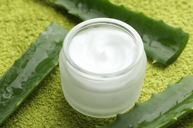 Photo of Cream and aloe leaves on green background, closeup