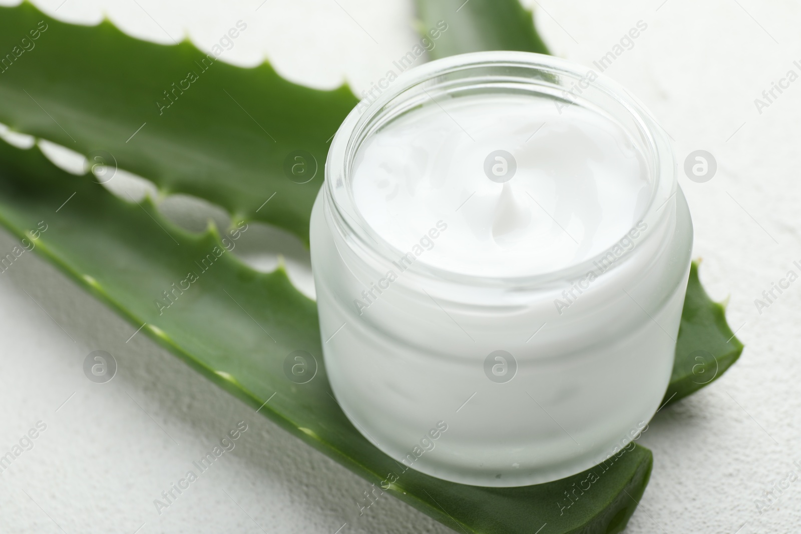 Photo of Cream and aloe leaves on white textured background, closeup