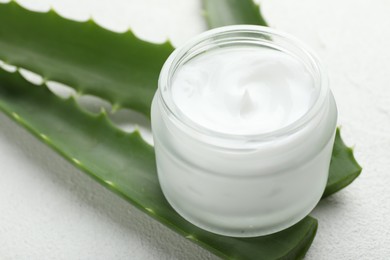 Photo of Cream and aloe leaves on white textured background, closeup