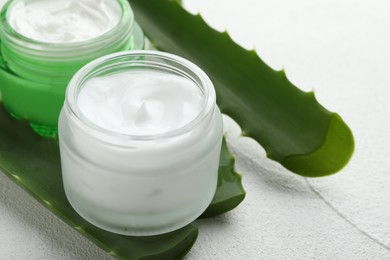 Photo of Cream and aloe leaves on white textured background, closeup