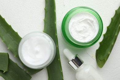 Cosmetic products and aloe leaves on white textured background, flat lay