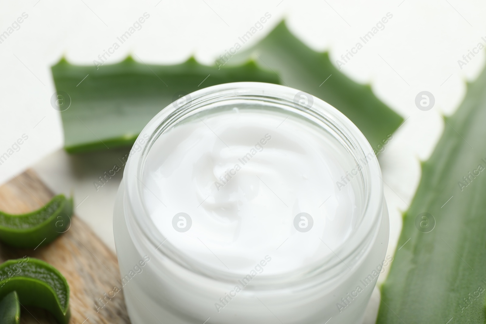 Photo of Cream and aloe leaves on white background, closeup