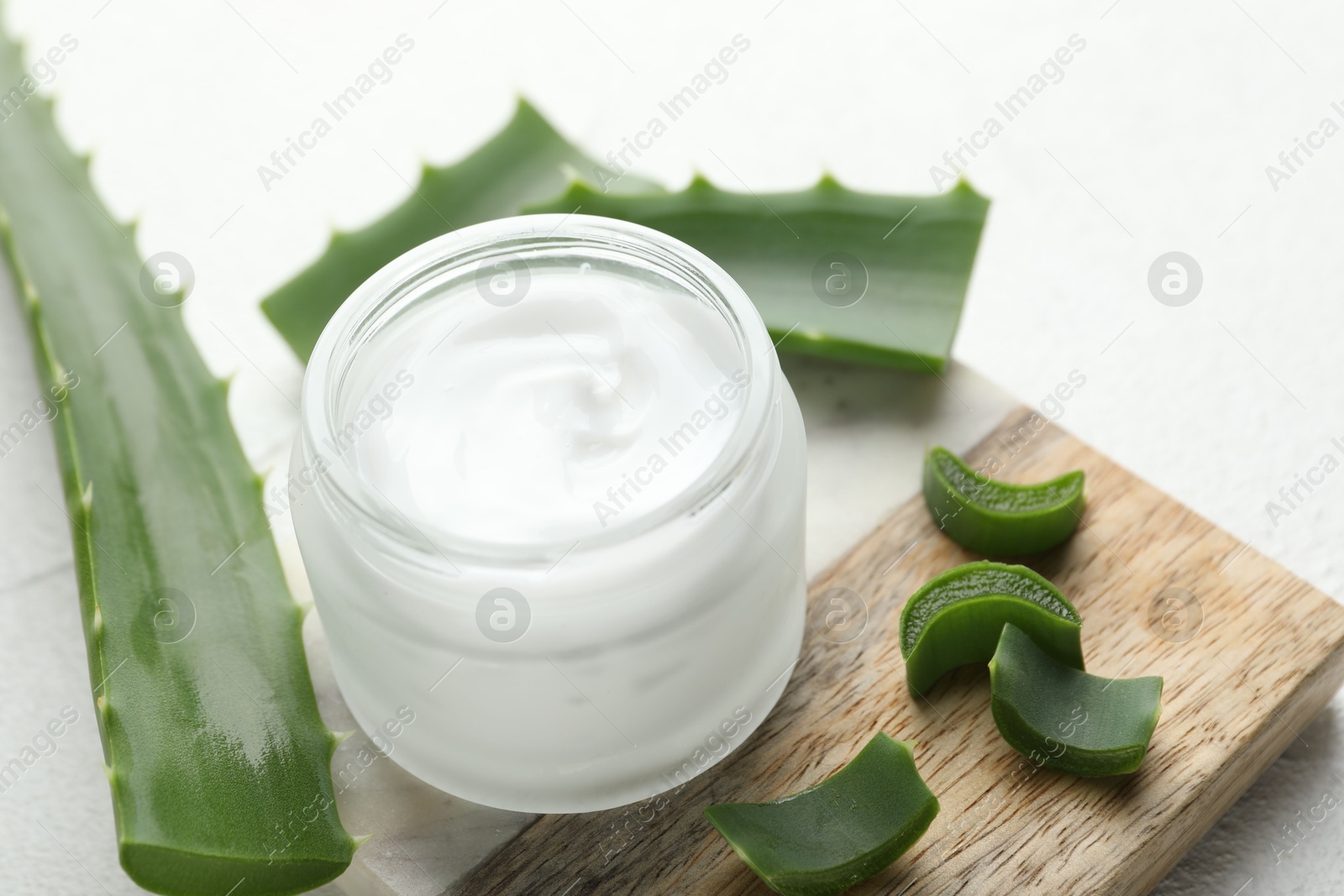 Photo of Cream and aloe leaves on white textured background, closeup