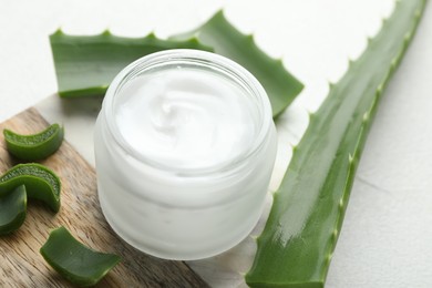 Photo of Cream and aloe leaves on white textured background, closeup