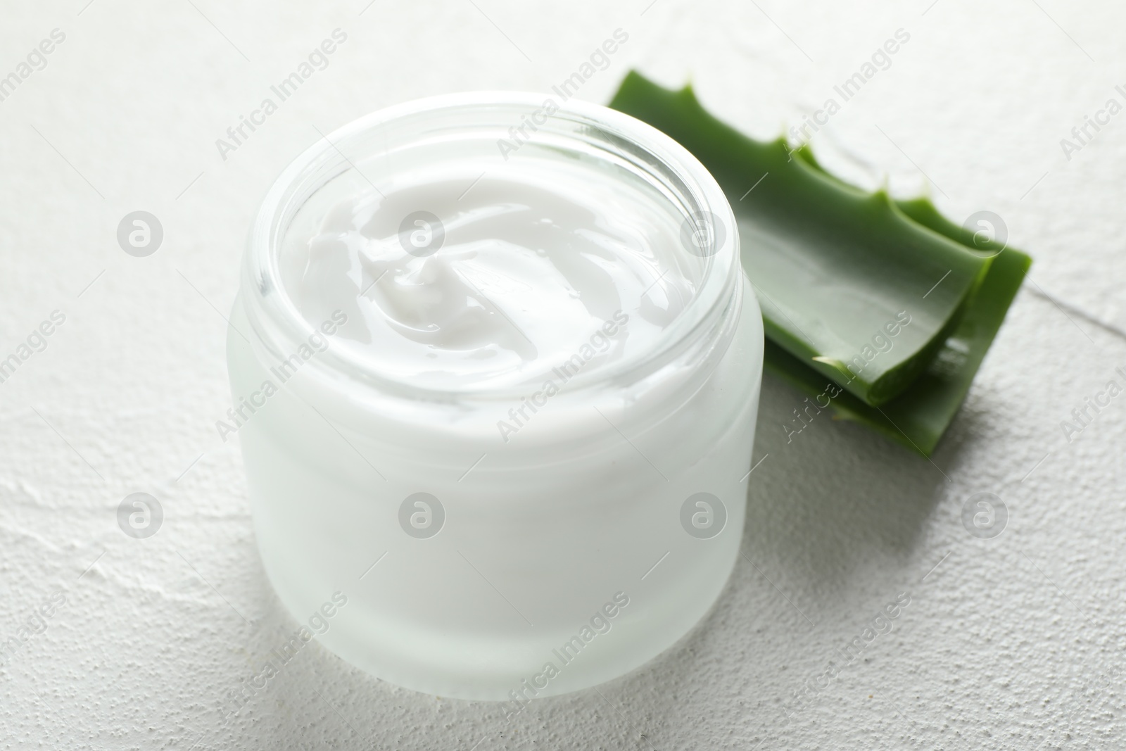 Photo of Cream and aloe leaves on white textured background, closeup