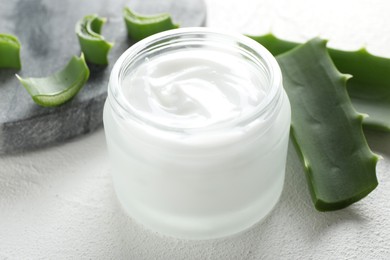 Photo of Cream and aloe leaves on white textured background, closeup