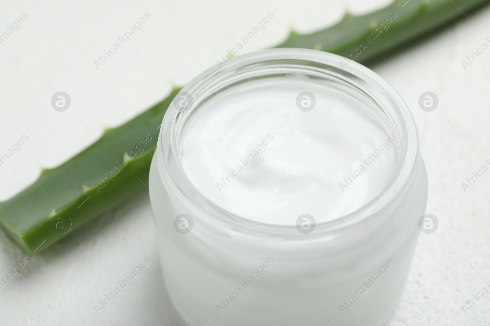 Photo of Cream and aloe leaves on white textured background, closeup