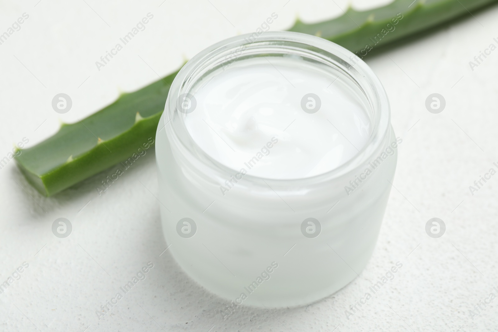 Photo of Cream and aloe leaves on white textured background, closeup