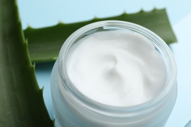 Photo of Cream and aloe leaves on light blue background, closeup