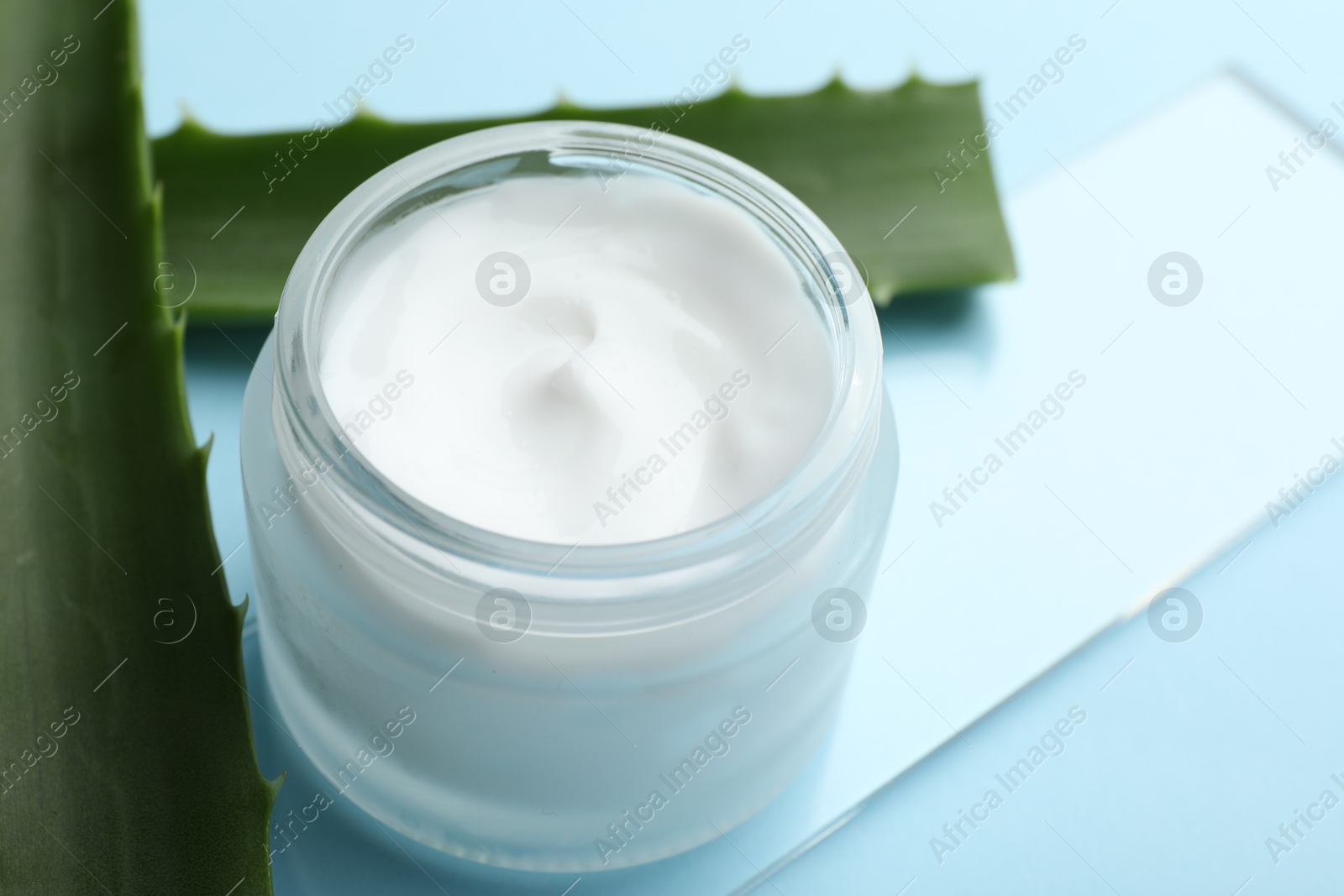 Photo of Cream and aloe leaves on light blue background, closeup