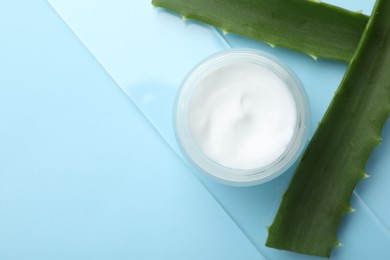 Photo of Cream and aloe leaves on light blue background, flat lay. Space for text