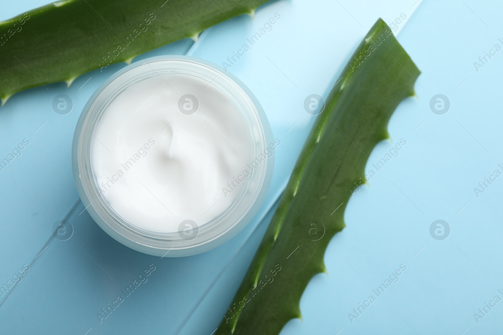 Photo of Cream and aloe leaves on light blue background, flat lay