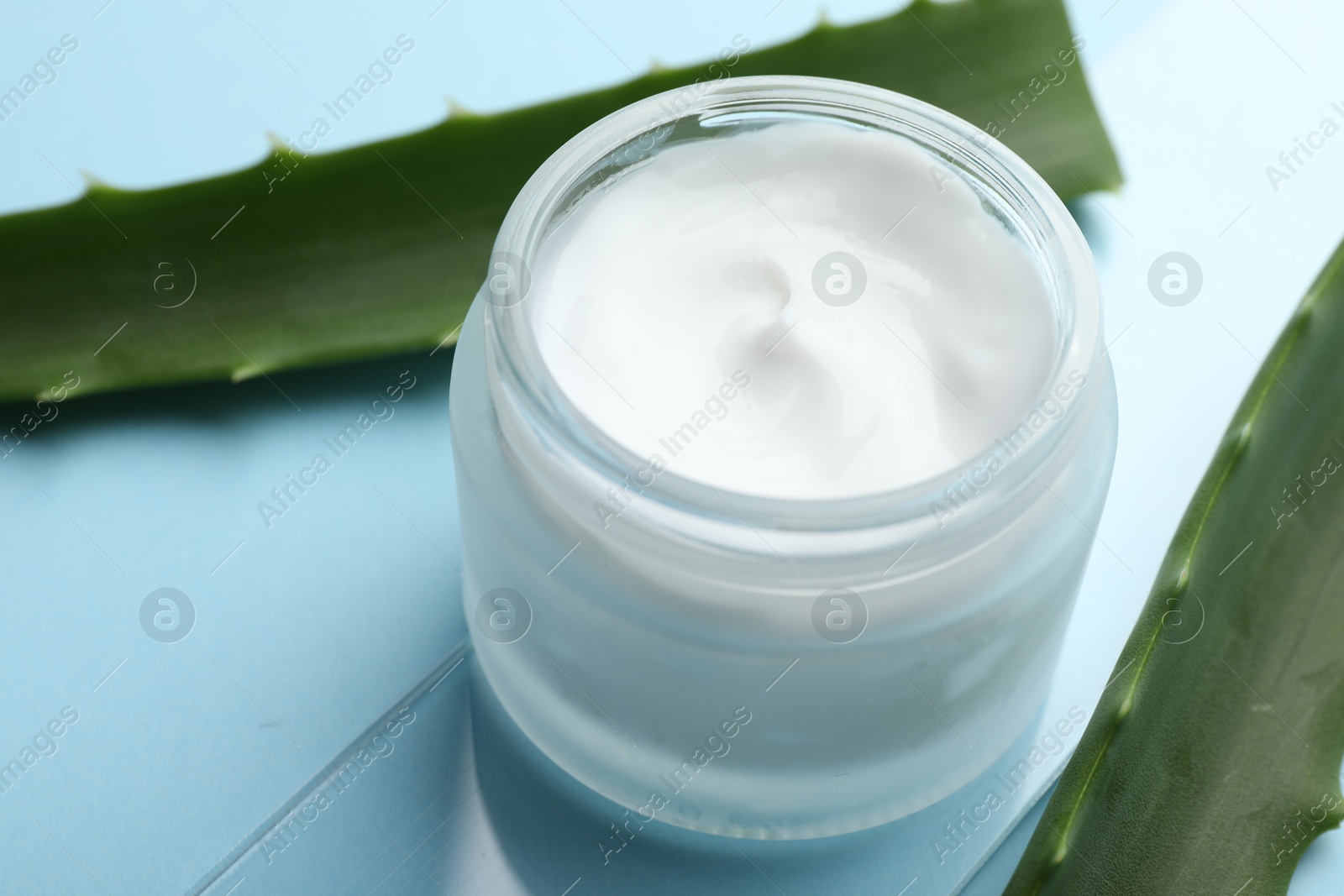 Photo of Cream and aloe leaves on light blue background, closeup