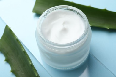 Photo of Cream and aloe leaves on light blue background, closeup