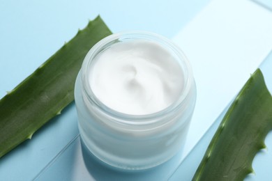 Cream and aloe leaves on light blue background, closeup