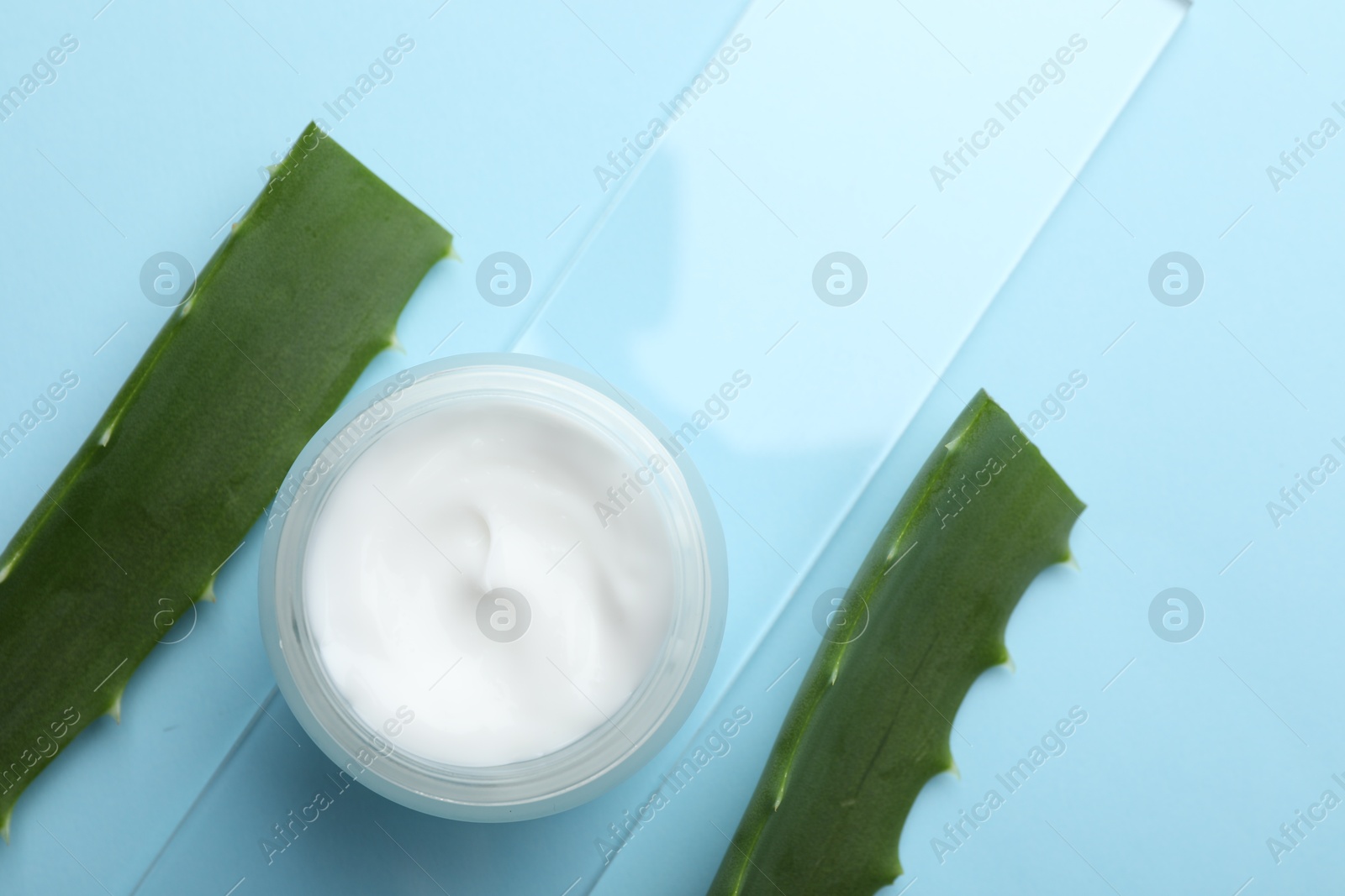 Photo of Cream and aloe leaves on light blue background, flat lay. Space for text