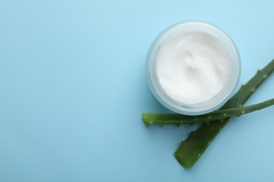 Photo of Cream and aloe leaves on light blue background, flat lay. Space for text