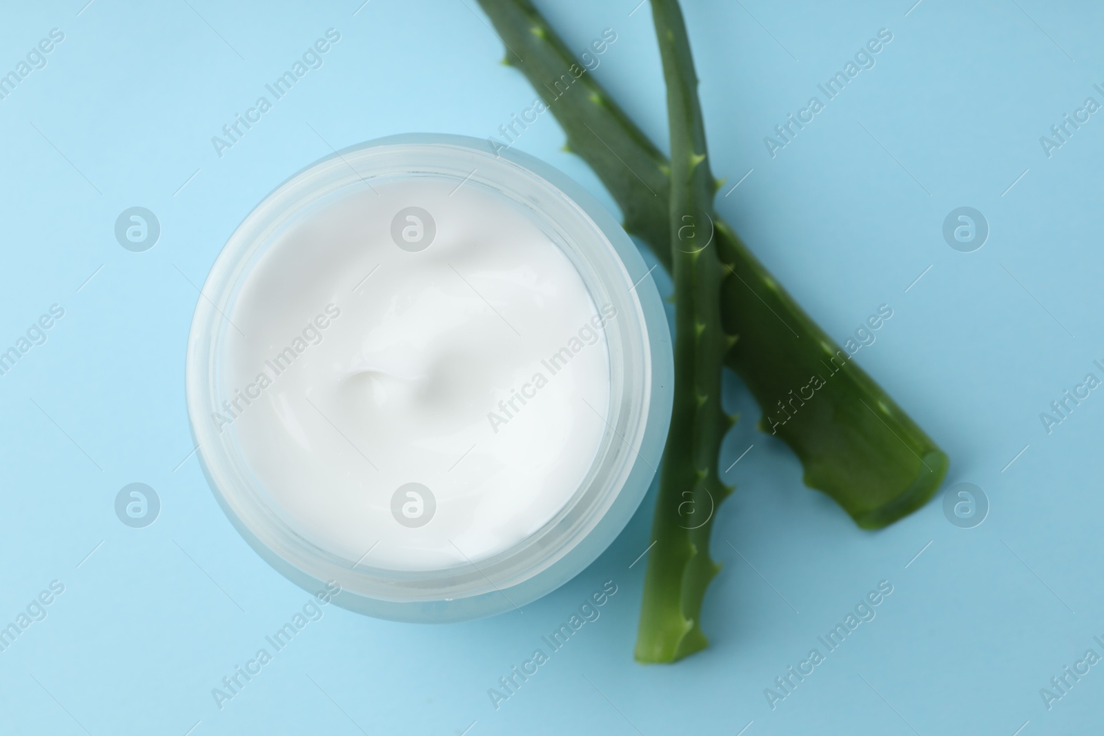 Photo of Cream and aloe leaves on light blue background, flat lay