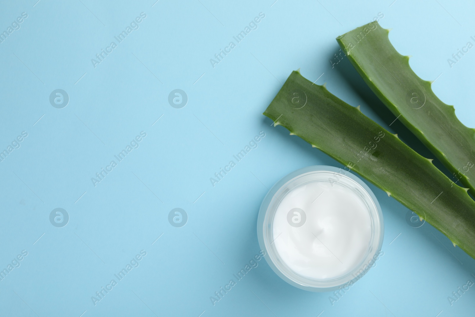 Photo of Cream and aloe leaves on light blue background, flat lay. Space for text