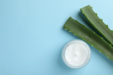 Photo of Cream and aloe leaves on light blue background, flat lay. Space for text