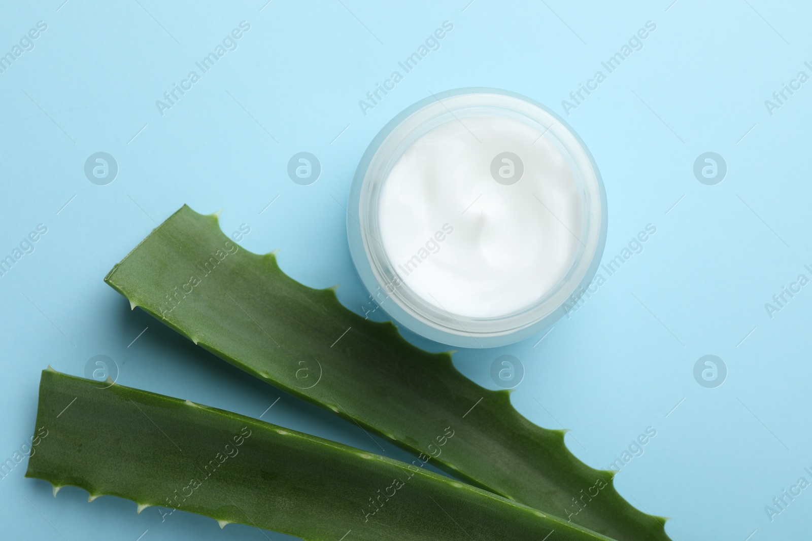 Photo of Cream and aloe leaves on light blue background, flat lay