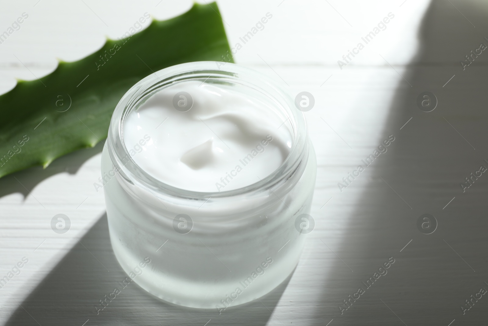 Photo of Cream and aloe leaves on white wooden background, closeup