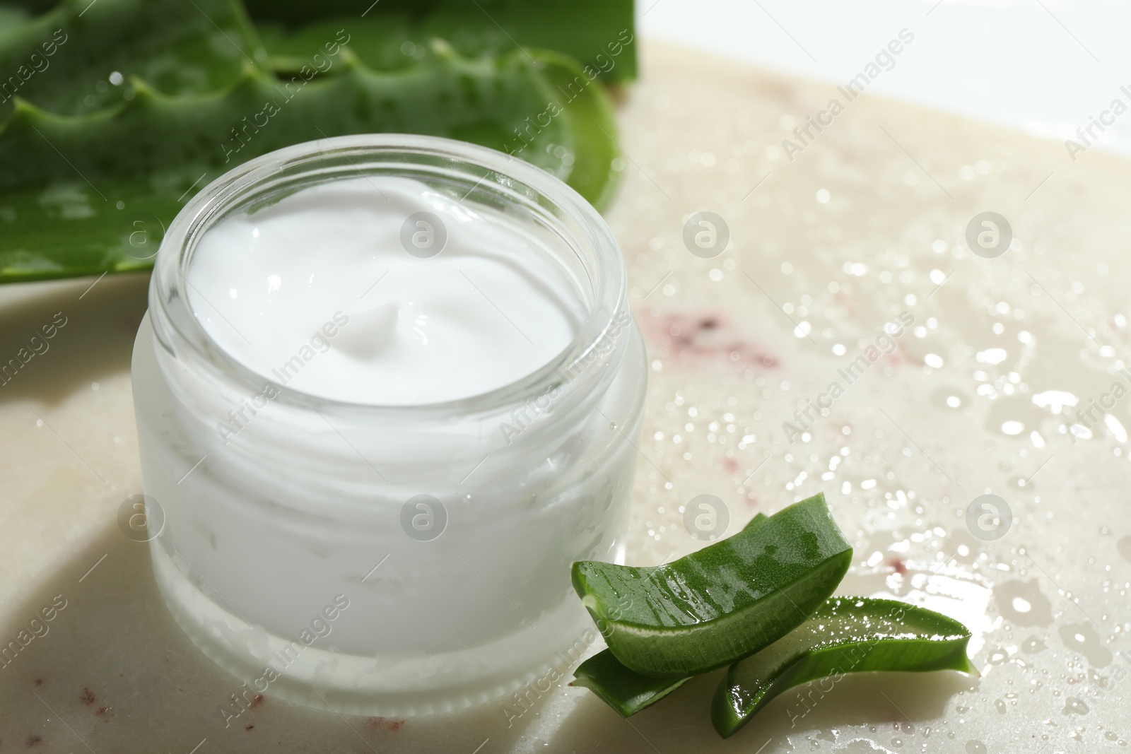 Photo of Cream and aloe leaves on light background, closeup. Space for text