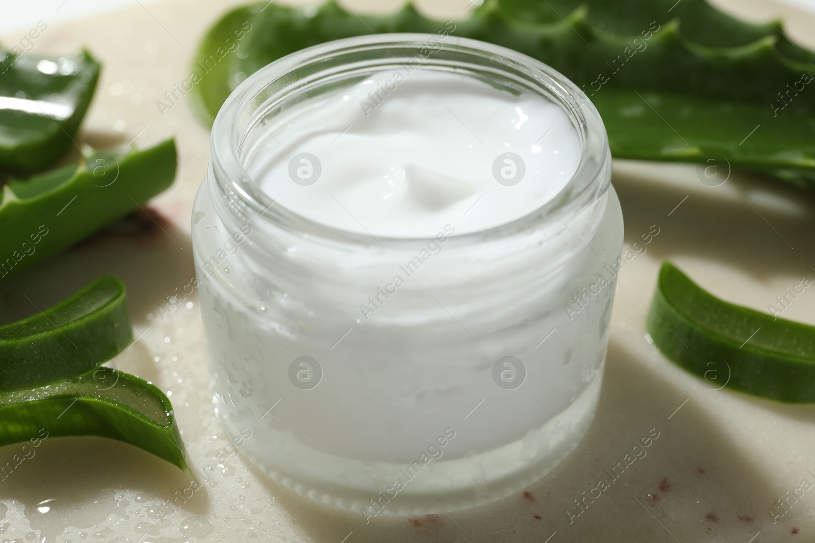 Photo of Cream and aloe leaves on light background, closeup