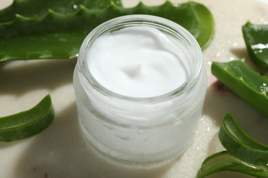 Photo of Cream and aloe leaves on light background, closeup