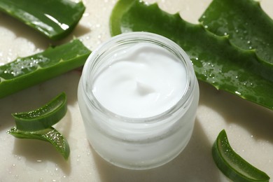 Photo of Cream and aloe leaves on light background, closeup