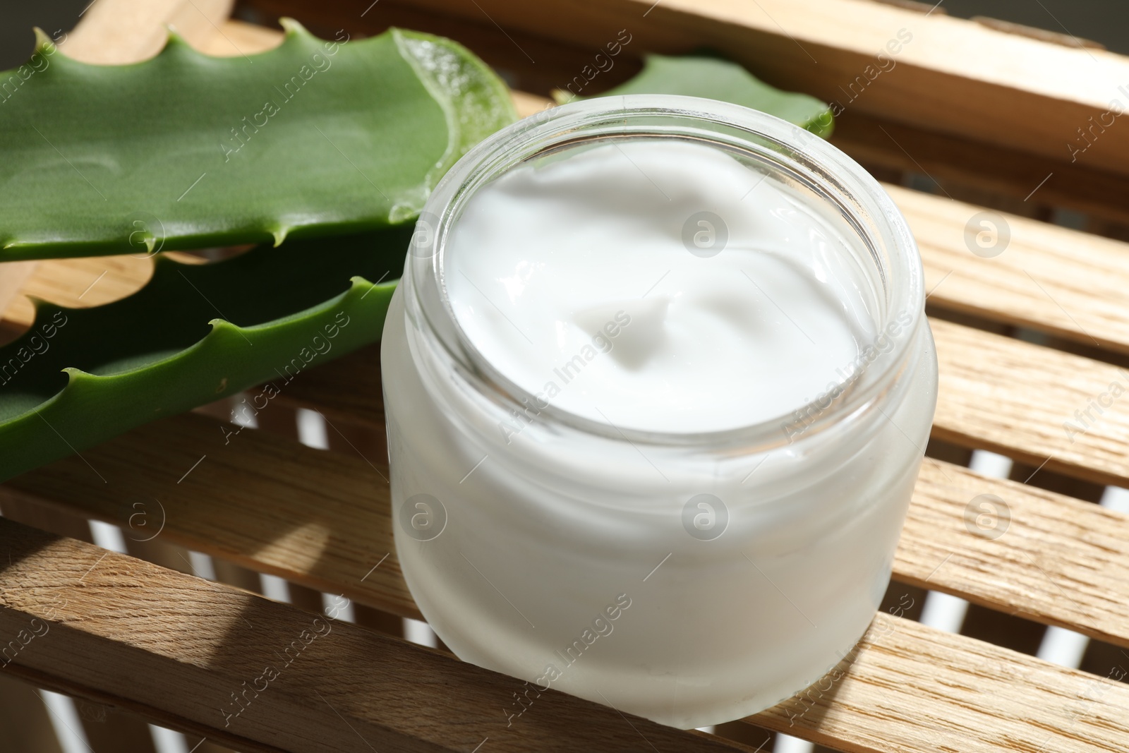 Photo of Cream and aloe leaves on wooden background, closeup