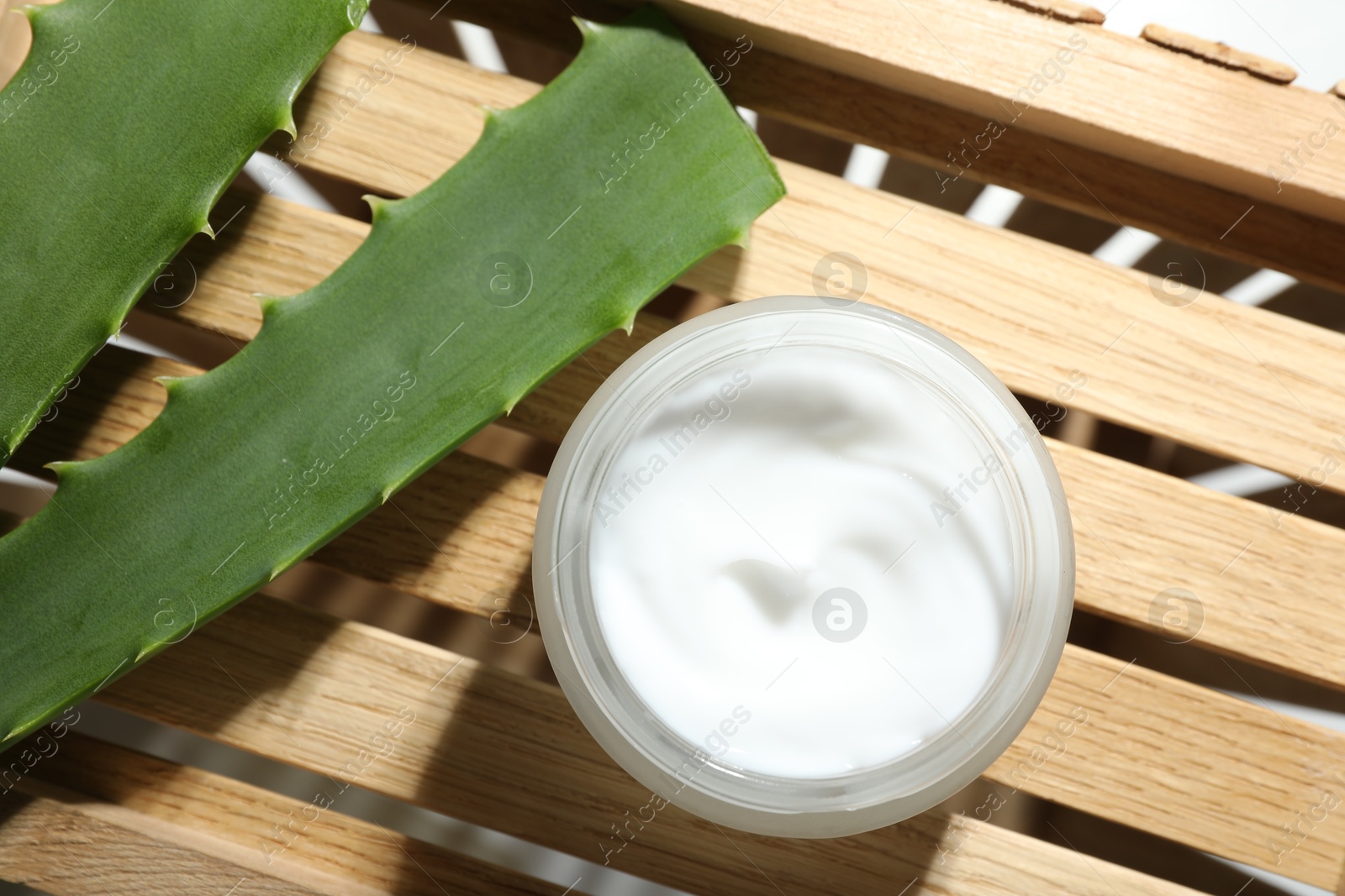 Photo of Cream and aloe leaves on wooden background, flat lay