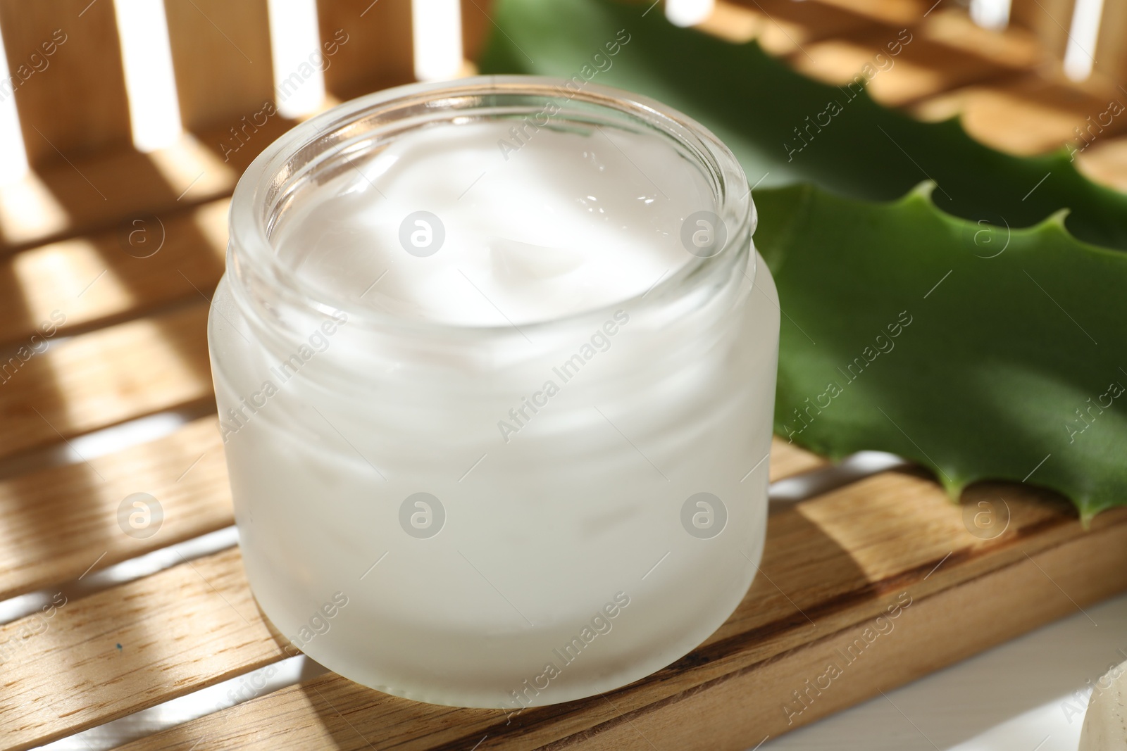 Photo of Cream and aloe leaves on wooden background, closeup