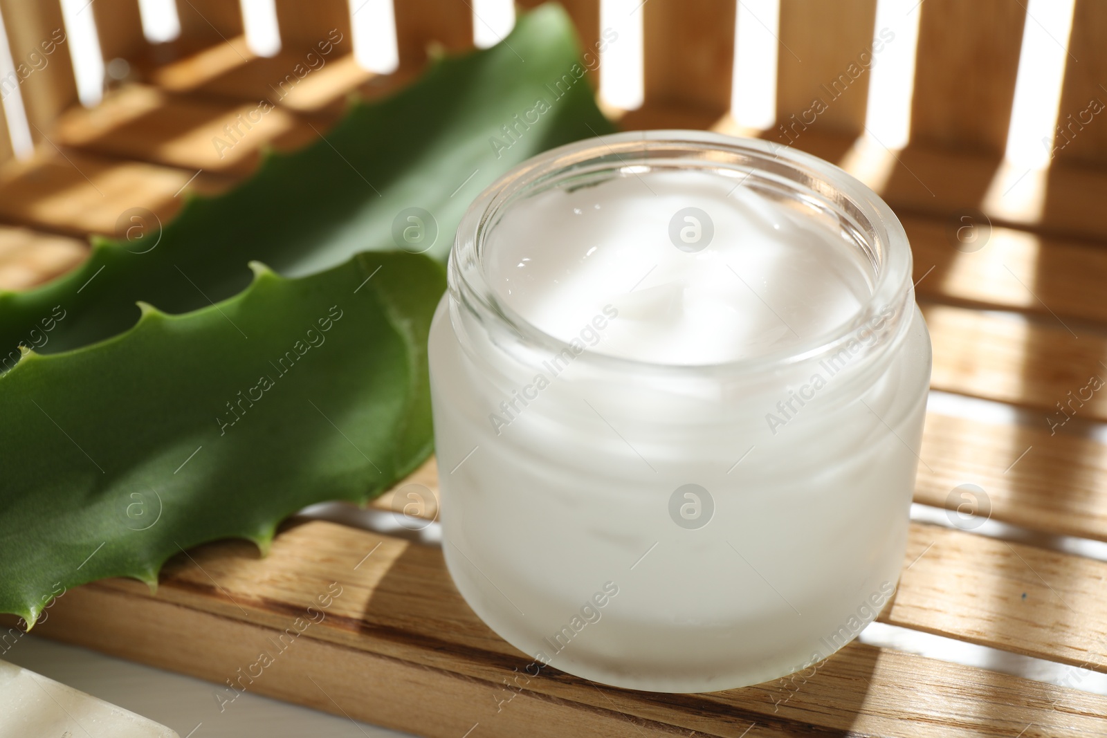 Photo of Cream and aloe leaves on wooden background, closeup