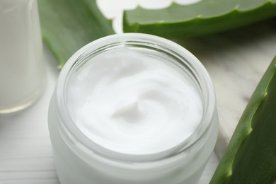 Photo of Cream and aloe leaves on white wooden background, closeup