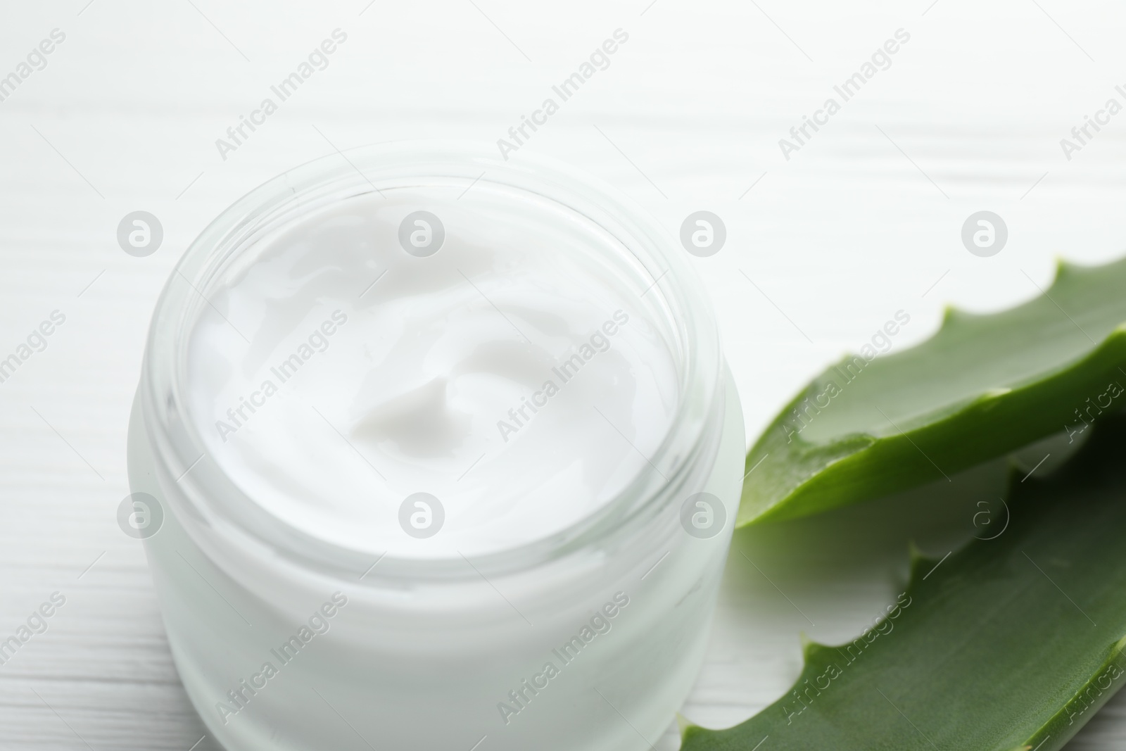 Photo of Cream and aloe leaves on white wooden background, closeup