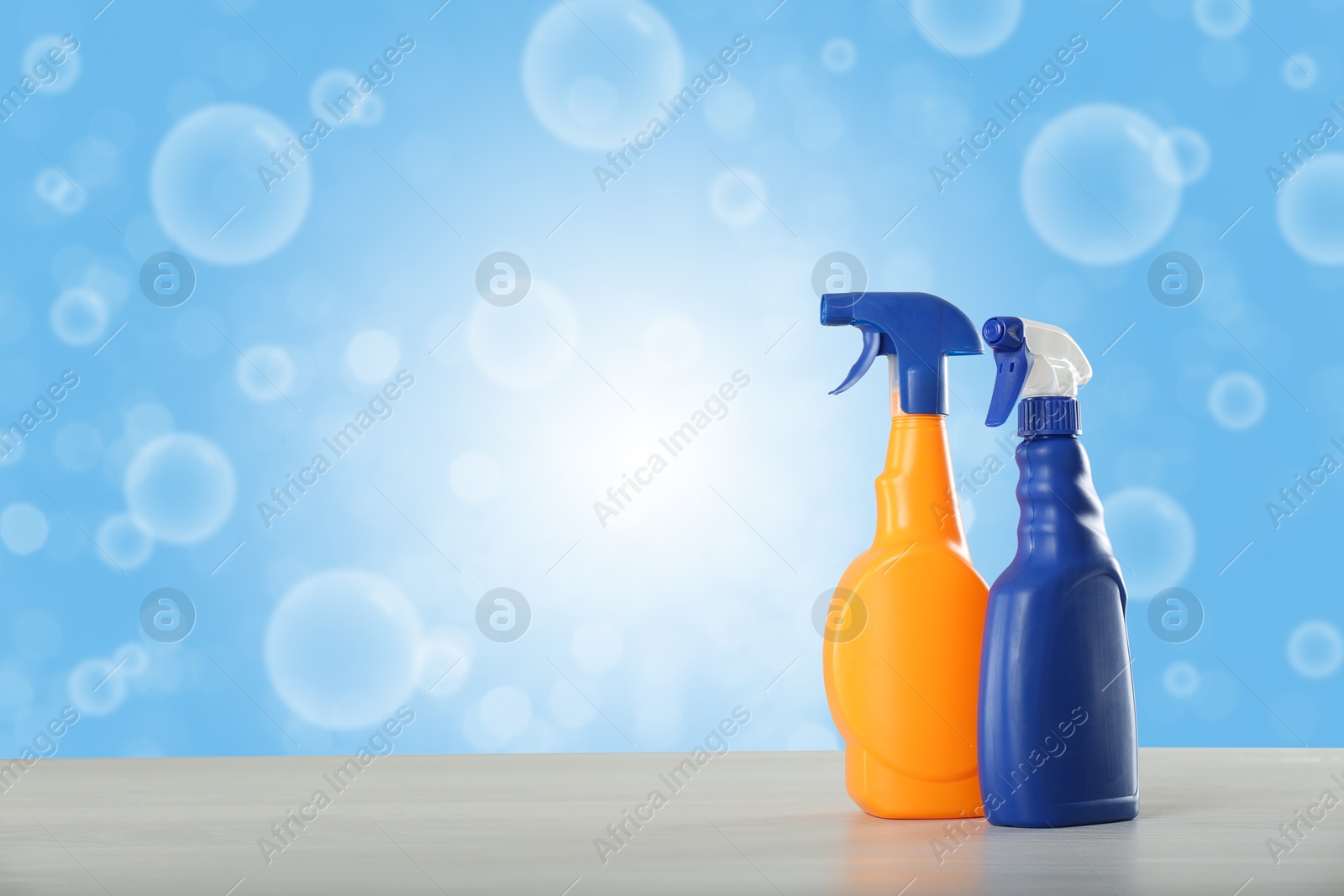 Image of Bottles of cleaning products on wooden table and soap bubbles against light blue gradient background, space for text. Bokeh effect