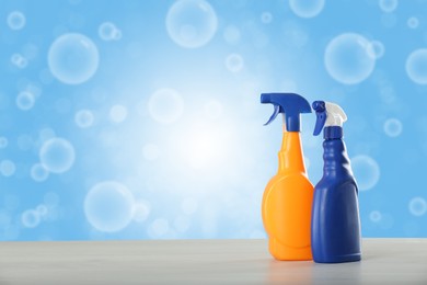 Bottles of cleaning products on wooden table and soap bubbles against light blue gradient background, space for text. Bokeh effect