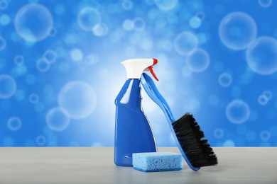 Image of Cleaning product and supplies on wooden table and soap bubbles against blue background, bokeh effect