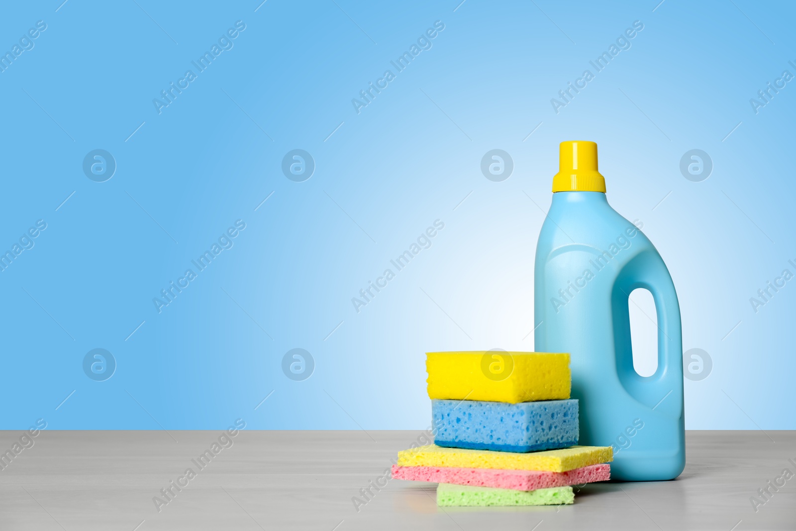 Image of Cleaning product and supplies on wooden table against light blue gradient background, space for text