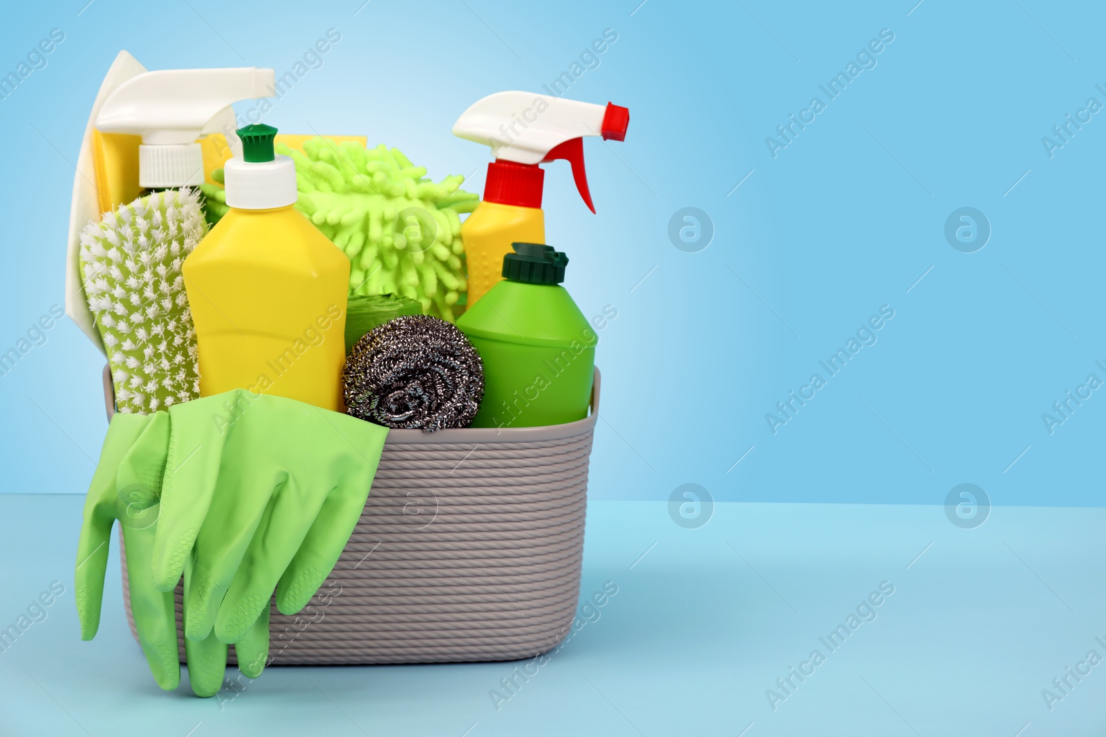 Image of Different cleaning products and supplies in basket on light blue gradient background, space for text